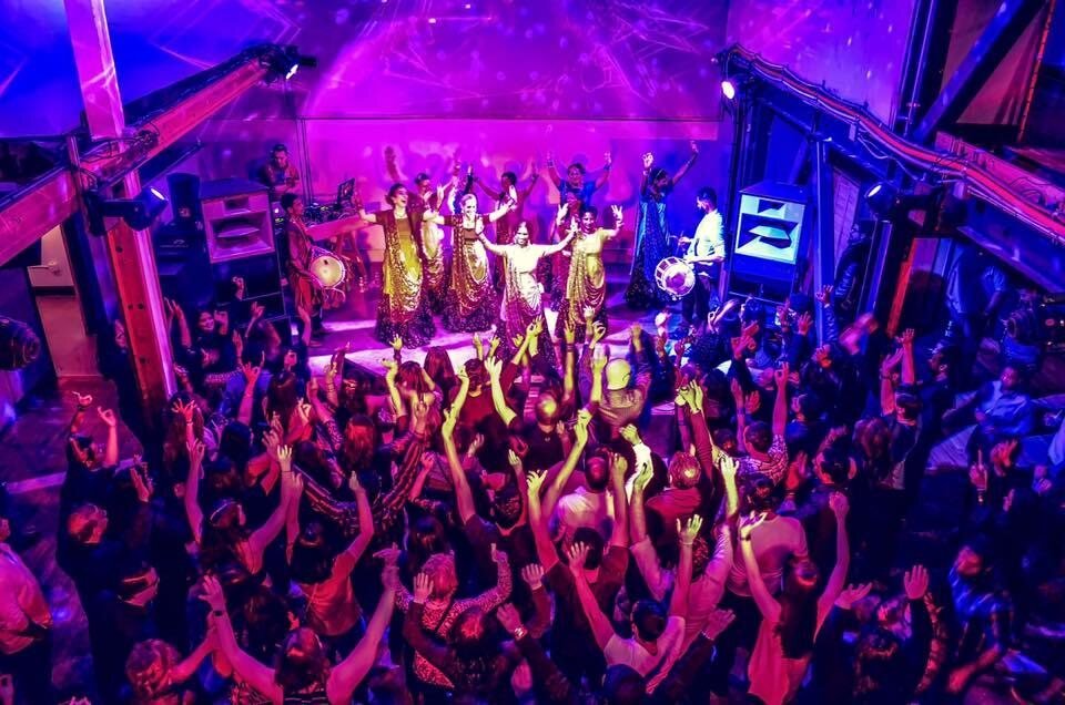 Crowd dancing in front of a stage with Bollywood dancers